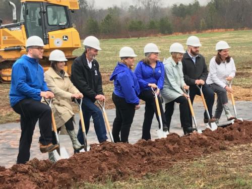 People in hard hats posing for a photo with their shovels in the dirt